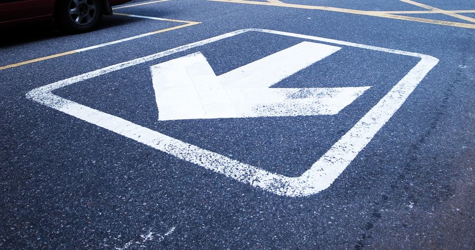 Close-up shot of a white arrow painted on asphalt indicating direction.