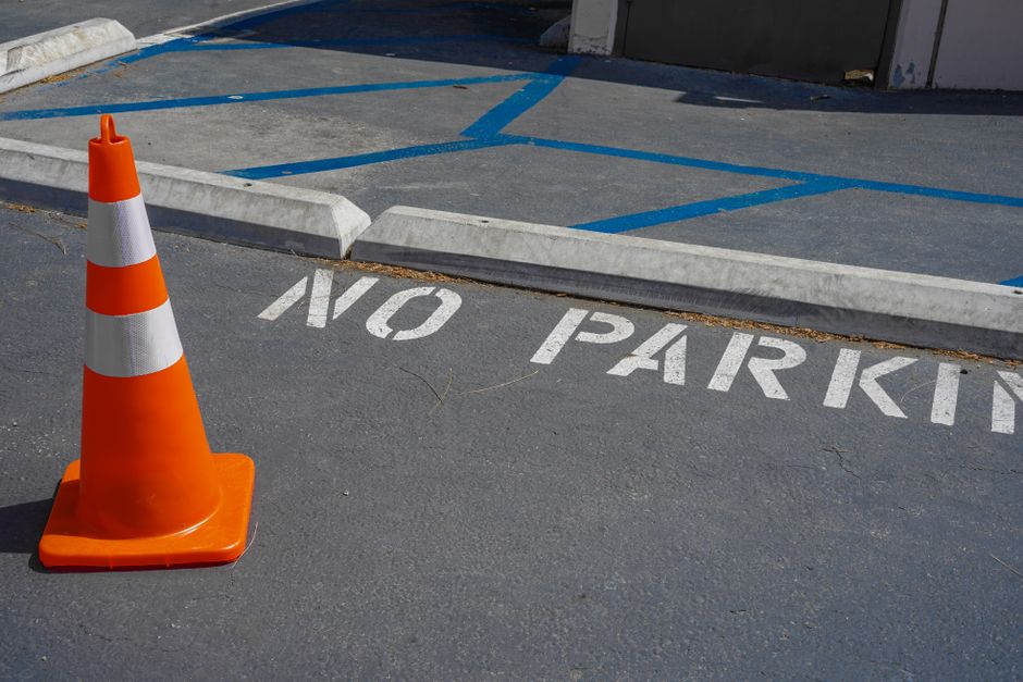 An orange traffic cone on a no parking zone with blue lines in a city street.