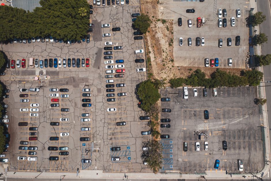 Aerial drone shot of urban parking lot filled with parked cars, showcasing urban infrastructure.