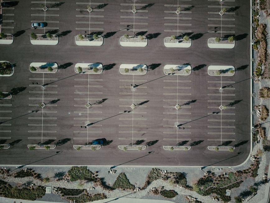 Drone aerial view of an empty parking lot with trees and shadows, creating a geometric pattern.